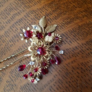 Peut inclure: &Eacute;pingle &agrave; cheveux dor&eacute;e avec un motif floral. L'&eacute;pingle pr&eacute;sente des accents de cristaux rouges et transparents, avec un groupe de pierres pr&eacute;cieuses rouges et de feuilles dor&eacute;es. L'accessoire pour cheveux est con&ccedil;u avec deux longues et fines &eacute;pingles dor&eacute;es.