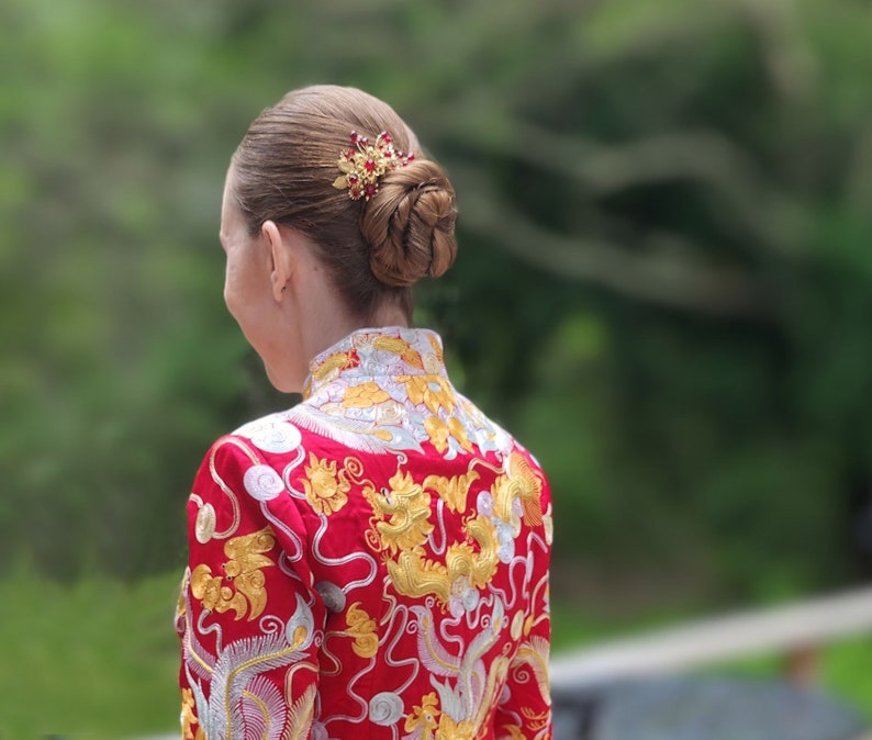 Peut inclure: Coiffure en chignon orn&eacute;e d'une barrette dor&eacute;e et rouge. La femme porte une veste rouge avec des broderies dor&eacute;es et argent&eacute;es repr&eacute;sentant des motifs de dragon et de ph&eacute;nix, un design traditionnel.