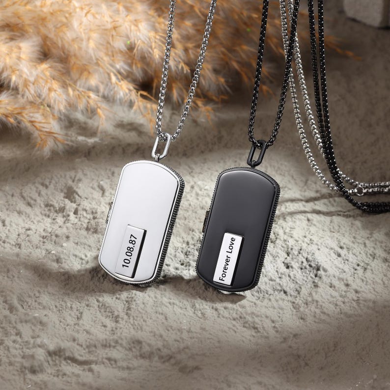 May include: Two rectangular pendant necklaces, one silver and one black, hang on delicate chains. The silver pendant displays the date "10.08.87", while the black pendant reads "Forever Love". Both pendants have a sleek, modern design.