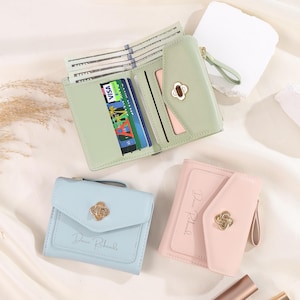 Op de afbeelding: Drie kleine portemonnees in pastelkleuren worden getoond. Eén is open en onthult contant geld en creditcards. De portemonnees zijn lichtgroen, lichtblauw en roze. Elke portemonnee heeft een goudkleurige sluiting en de naam "Davie Richards" staat op de blauwe en roze portemonnees.