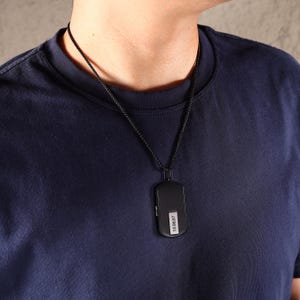 May include: A black pendant necklace with a rectangular pendant. The pendant has a small white label with the numbers "10.08.87" printed on it. The necklace chain is also black.