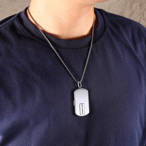May include: Silver dog tag pendant necklace with the words "Forever Love" engraved on the front. The pendant hangs from a delicate chain. The person in the image is wearing a navy blue t-shirt.