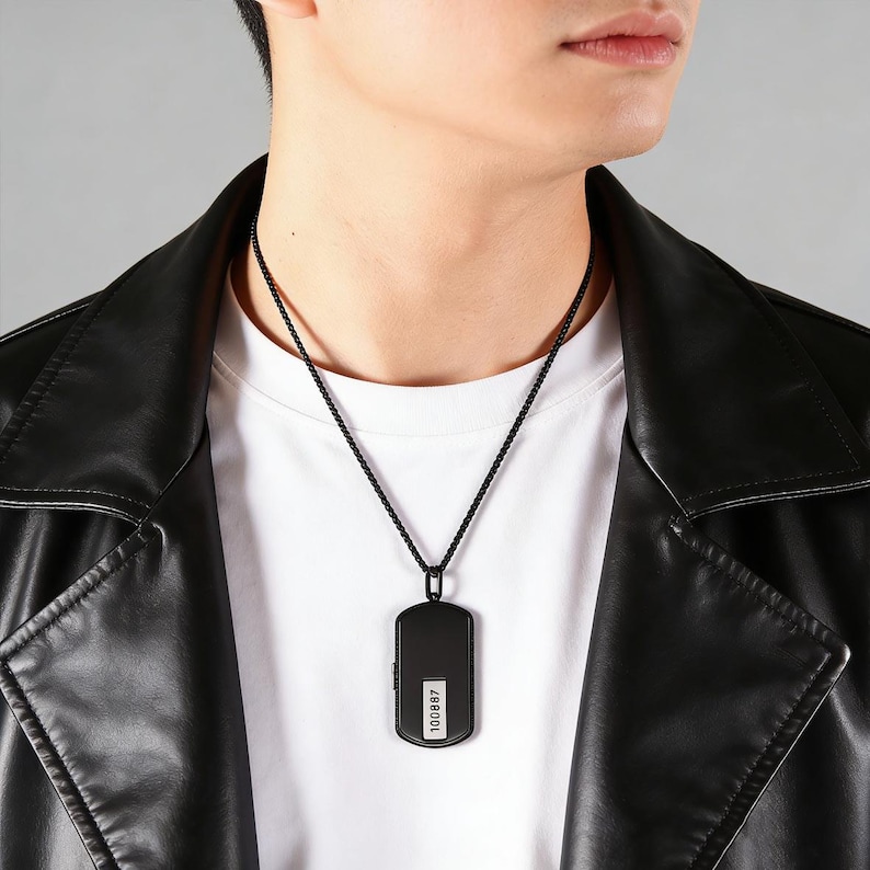 May include: A black dog tag pendant necklace. The rectangular pendant has a small white section with the number "100887" printed on it. The necklace chain is also black.