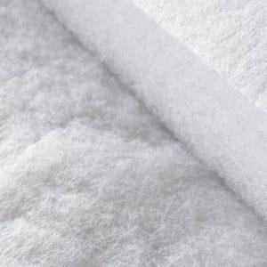 Puede incluir: Un material de relleno blanco, fibroso y grueso, con una textura suave y esponjosa. El material est&aacute; doblado, revelando una secci&oacute;n transversal densa y estratificada de fibras sint&eacute;ticas blancas que parecen ligeras y porosas.