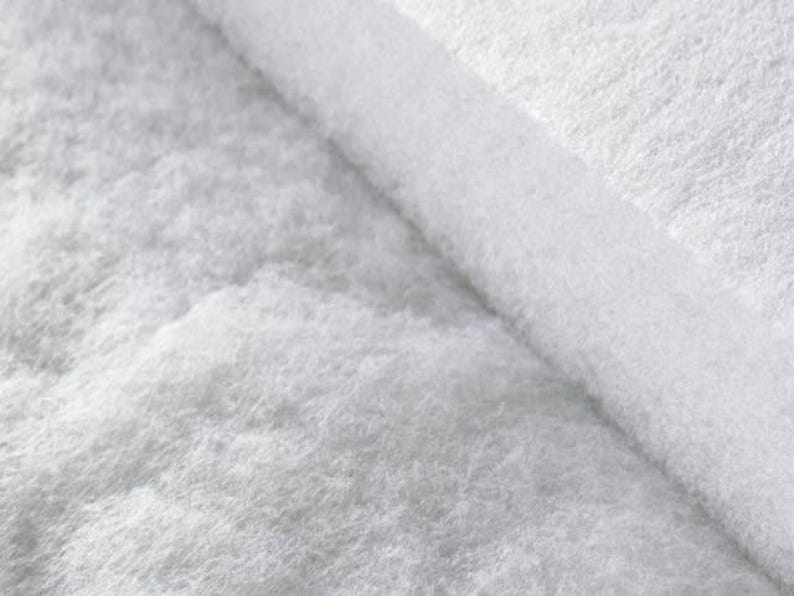 Puede incluir: Un material de relleno blanco, fibroso y grueso, con una textura suave y esponjosa. El material est&aacute; doblado, revelando una secci&oacute;n transversal densa y estratificada de fibras sint&eacute;ticas blancas que parecen ligeras y porosas.