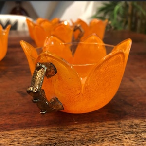 May include: Set of four orange glass tulip-shaped bowls with gold metal handles. The bowls are perfect for serving snacks or desserts.