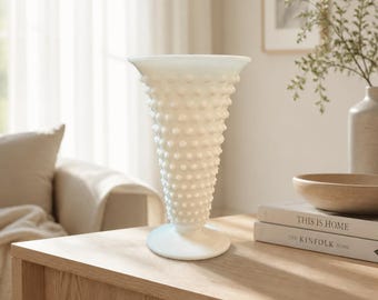 Può includere: Un vaso in vetro opalino bianco con bordo svasato e una texture a rilievo con motivo a pois su tutta la superficie esterna. Il vaso presenta un corpo conico che si restringe verso la base, poggiando su un piedistallo circolare.