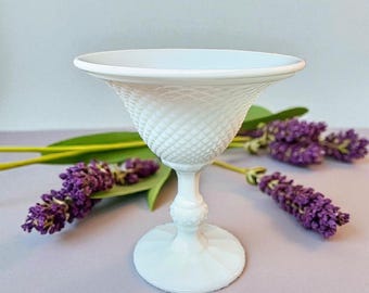 Può includere: Un calice di vetro bianco in stile vintage con un motivo a diamante strutturato sulla coppa. Il calice poggia su una base rotonda e ha un gambo delicato. Rametti di lavanda viola e foglie verdi sono disposti attorno al calice.