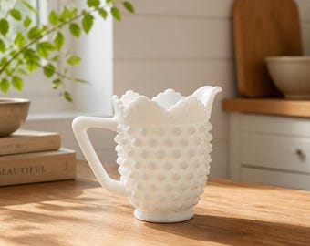 Può includere: Una brocca in vetro opalino bianco con una texture a pois in rilievo su tutto il corpo, un bordo smerlato e un manico robusto. La brocca presenta una finitura lucida e un ampio beccuccio, mostrando un design classico con base arrotondata.