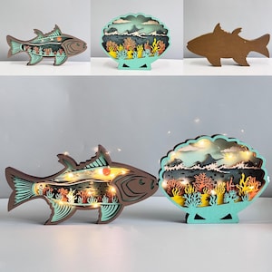 May include: Wooden decorative lights in the shape of a fish and a seashell. The fish is brown with teal details, featuring a layered underwater scene. The seashell design includes coral and fish. Both have small fairy lights.