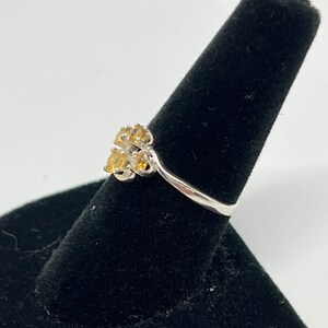 May include: A silver ring with a cluster of yellow gemstones set in a flower shape.