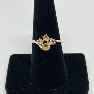 May include: A silver ring with a cluster of five yellow gemstones set in a curved band.