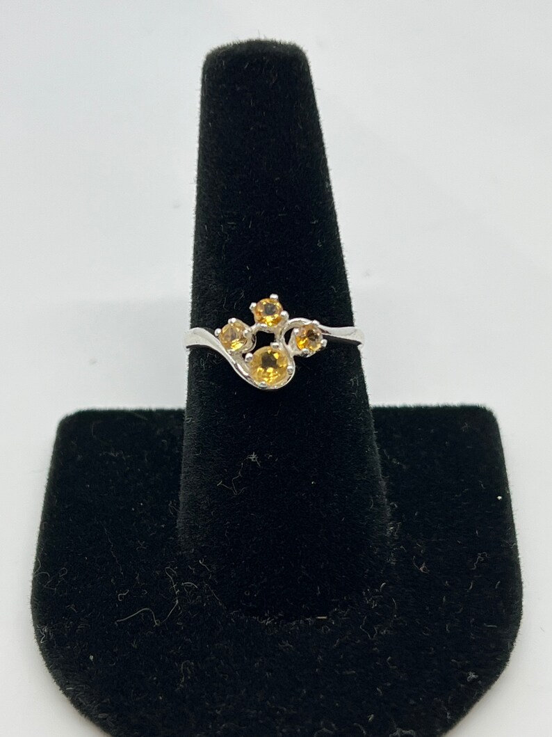 May include: A silver ring with a cluster of five yellow gemstones set in a curved band.
