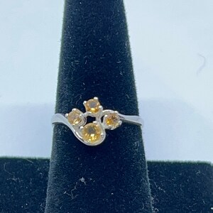 May include: A silver ring with a cluster of four small, round, orange gemstones set in a wavy band.