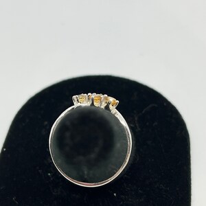 May include: A silver ring with three small, round, yellow gemstones set in a row.
