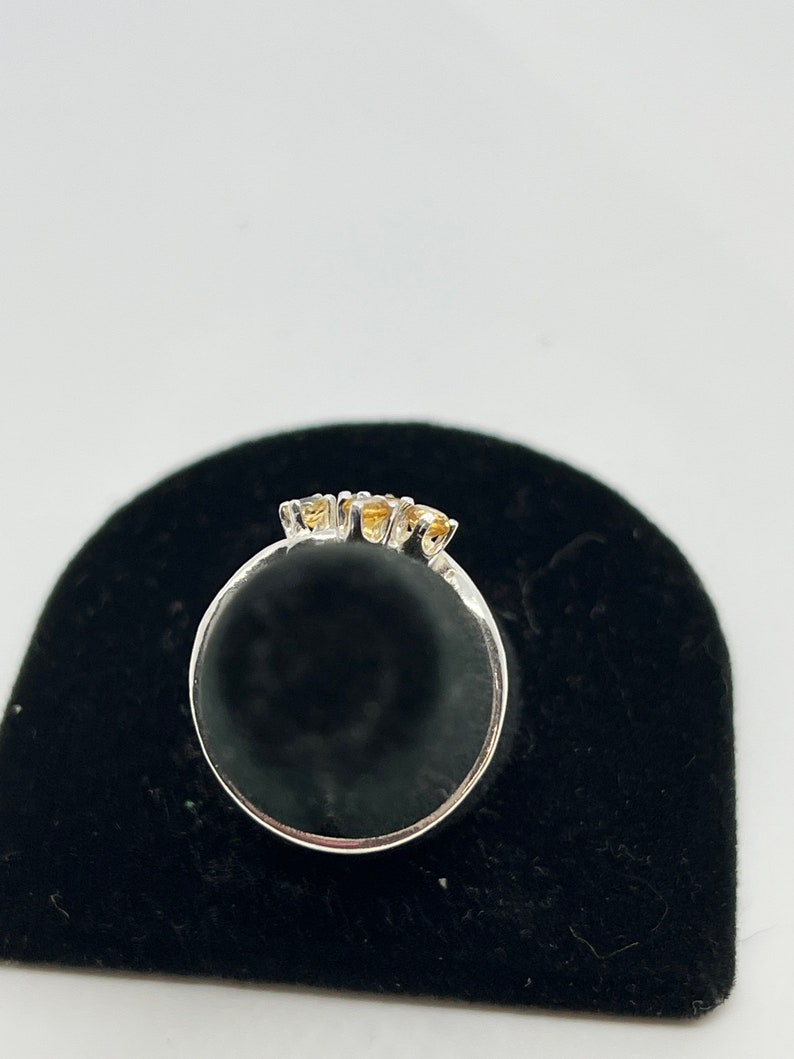 May include: A silver ring with three small, round, yellow gemstones set in a row.
