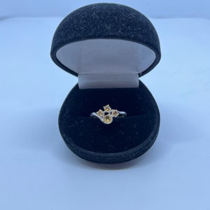 May include: A silver ring with a cluster of five yellow gemstones set in a curved design. The ring is displayed in a black velvet ring box.