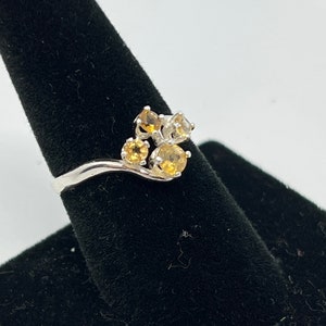 May include: A silver ring with a cluster of five round gemstones. The gemstones are a mix of yellow and white.