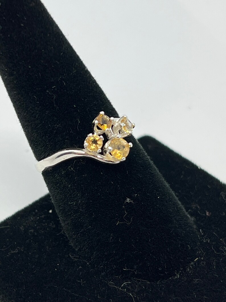 May include: A silver ring with a cluster of five round gemstones. The gemstones are a mix of yellow and white.
