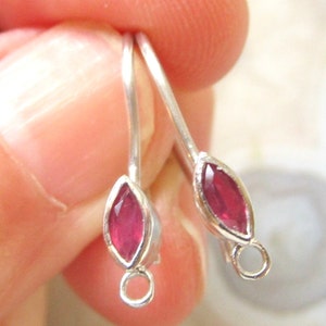 May include: A pair of silver earrings with a marquise-shaped, deep red gemstone. The earrings have a simple, elegant design with a hook closure. The gemstones are set in a silver bezel.