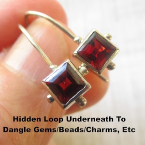 May include: A pair of silver earrings with square, deep red gemstones. Each earring features a square gemstone set in a silver frame, with small silver accents. The earrings have a hook design. The text in the image says "Hidden Loop Underneath To Dangle Gems/Beads/Charms, Etc."