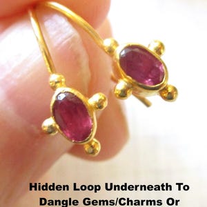 Peut inclure: Boucles d'oreilles dorées avec des pierres précieuses ovales de couleur rubis. Chaque boucle d'oreille présente une pierre centrale entourée de petits accents dorés. Texte sur l'image : Hidden Loop Underneath To Dangle Gems/Charms Or Wear As Shown.