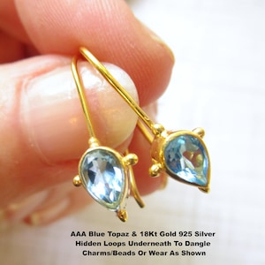 May include: A pair of gold-colored earrings with teardrop-shaped, light blue gemstones. The earrings have a hook design and small decorative accents. Text on the image reads: AAA Blue Topaz & 18Kt Gold 925 Silver Hidden Loops Underneath To Dangle Charms/Beads Or Wear As Shown.