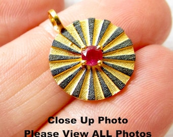 May include: Gold pendant with a black and gold sunburst design and a red gemstone in the center.