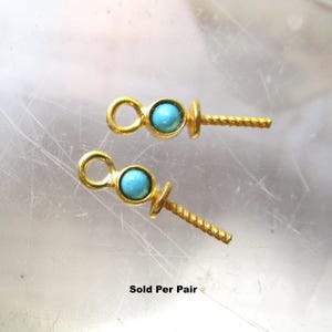 May include: Two gold-toned jewelry findings, each featuring a small circular turquoise bead set in a metal frame, a top loop for attachment, and a textured, pointed post for securing a pearl or bead. The text "Sold Per Pair" is visible below.
