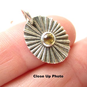 May include: Oval silver pendant with a sunburst design and a small, round, yellow gemstone in the centre. The pendant has a textured, ridged surface. The text "Close Up Photo" is at the bottom.