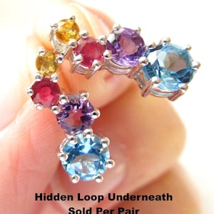May include: A pair of earrings with a curved design, featuring a series of colorful gemstones. The gemstones include yellow, red, purple, and blue hues, set in a silver metal. The text "Hidden Loop Underneath Sold Per Pair" is visible.
