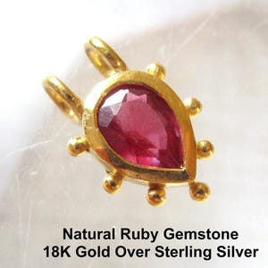 May include: A pear-shaped pendant featuring a faceted natural ruby gemstone set in 18K gold over sterling silver. The gold frame is accented with small spherical beads along the edges and includes two top loops. Text reads: Natural Ruby Gemstone 18K Gold Over Sterling Silver.