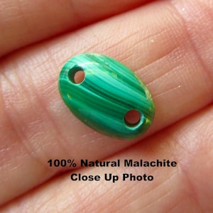 May include: Close-up of a green malachite bead with a natural, striped pattern. The oval bead has two holes for stringing. The text on the image reads "100% Natural Malachite Close Up Photo."