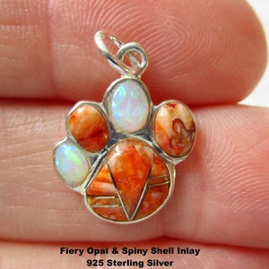 May include: A paw print shaped pendant crafted from 925 sterling silver, featuring an inlay of fiery orange spiny oyster shell and iridescent white opal stones. The text Fiery Opal & Spiny Shell Inlay 925 Sterling Silver is printed below.