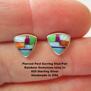 May include: A pair of triangular stud earrings featuring a multi-colored gemstone inlay set in 925 sterling silver. The inlay includes segments of white opal, green, purple, orange, and blue stones. Text reads: Pierced Post Earring Stud Pair Rainbow Gemstone Inlay In 925 Sterling Silver Handmade In USA.