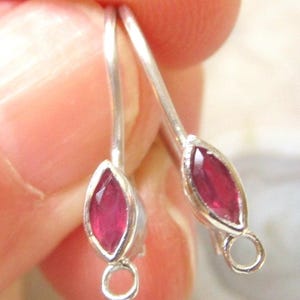 May include: A pair of silver earrings with a marquise-shaped, deep red gemstone. The gemstones are set in a silver bezel and have a loop at the bottom for attaching to a hook. The earrings are shown close up.