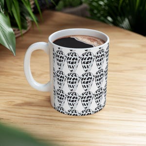 May include: White ceramic coffee mug with a black and white pattern of seashells. The mug is filled with coffee.