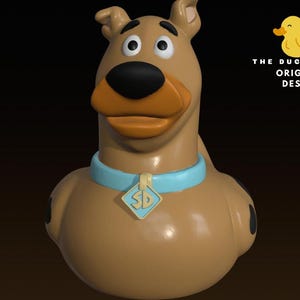 May include: A brown rubber duck shaped like a dog with a light blue collar and a diamond-shaped tag featuring the letters SD. The figure has a dark brown nose, black spots on its sides, and the text THE DUCK SHOP ORIGINAL DESIGN with a yellow duck icon.