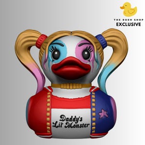 Op de afbeelding: Een nieuwigheid eendenbeeldje met een wit gezicht, blauwe en roze oogmake-up en rode lippen. De eend heeft blonde staartjes met rode en blauwe banden. De body is rood en blauw met de tekst "Daddy's Lil' Monster". Het logo The Duck Shop Exclusive staat rechtsboven.