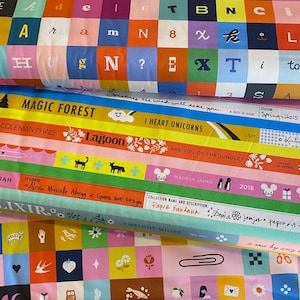 May include: A colorful assortment of fabric rolls with various patterns. One features a grid of letters and numbers, while others display text like "MAGIC FOREST" and "I HEART UNICORNS." The fabrics showcase a variety of designs and colors.