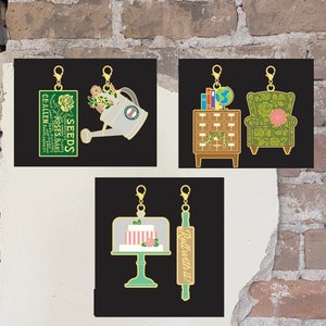 May include: Four gold zipper pulls with different designs. The first pull features a watering can with flowers and the text "Seeds Greenhouse Hardy Plants Roses Bulbs Potatoes Ce Allen Battleboro Northern", the second pull features a bookshelf with books and a globe, the third pull features a cake on a stand, and the fourth pull features a rolling pin with the text "Roll with it!"