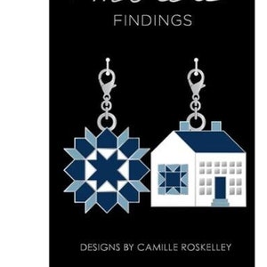 May include: A pair of silver dangle earrings with blue and white quilt block designs. One earring features a star block and the other a house block. The earrings are labeled "Moda Findings" and "Designs by Camille Roskelley".
