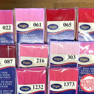 May include: Assortment of pink and red bias tape rolls with the brand name "Wrights" and product information, including the text "Bias Tape Extra Wide Double Fold".