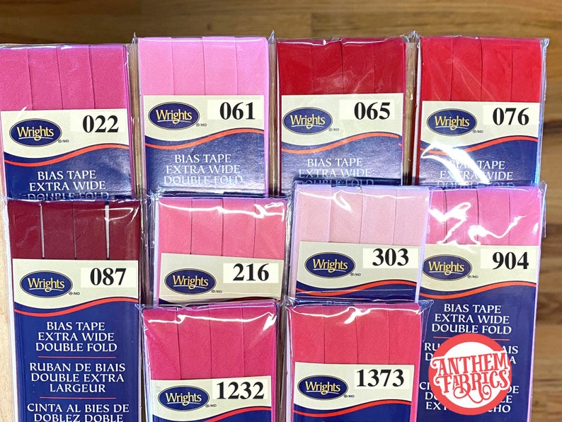 May include: Assortment of pink and red bias tape rolls with the brand name "Wrights" and product information, including the text "Bias Tape Extra Wide Double Fold".