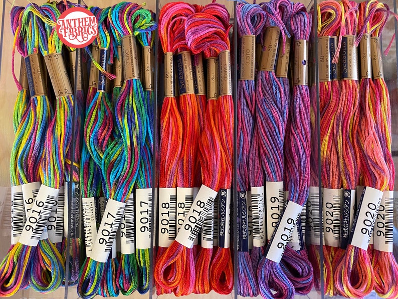 May include: A close-up of ten spools of colorful embroidery floss. The floss is arranged in rows, with each row containing a different color combination. The spools are labeled with the numbers 9016, 9017, 9018, 9019, and 9020.