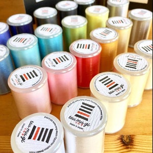 May include: A collection of spools of colorful cotton thread, each labeled with the text "tsu mu gi" and "Made in Japan".