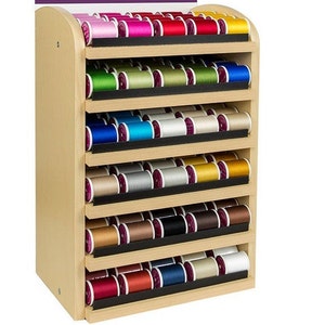 May include: A wooden thread storage rack with seven shelves. Each shelf is filled with spools of thread in various colors, including red, blue, green, yellow, and white.