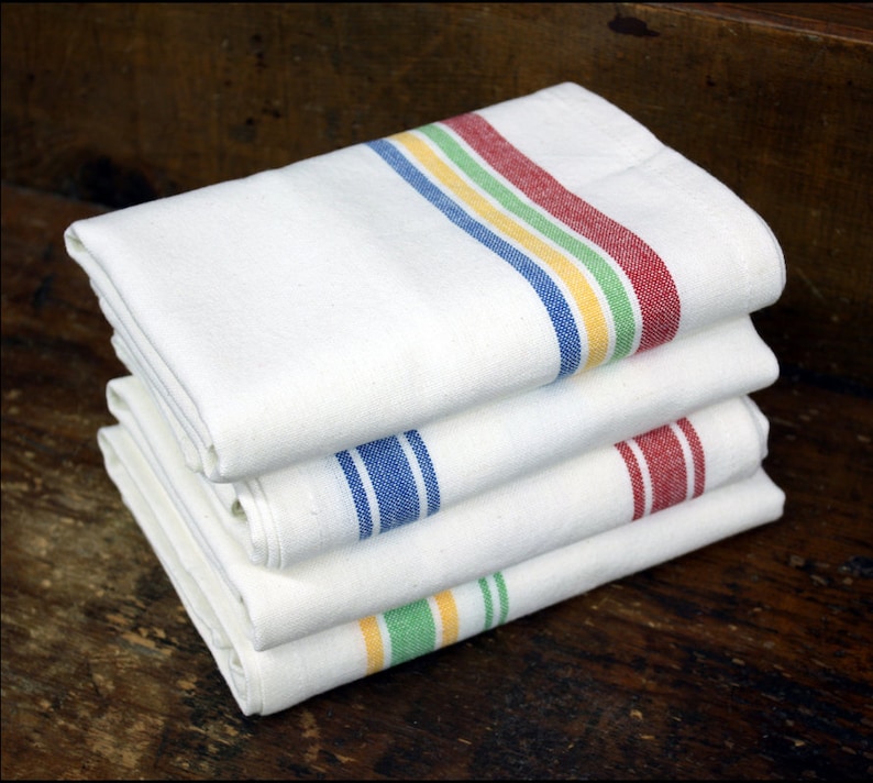 May include: A stack of four white kitchen towels with colored stripes. The top towel has red, yellow, and green stripes. The second towel has blue stripes. The third towel has red stripes. The bottom towel has green and yellow stripes.