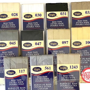 May include: A collection of bias tape in various colors, including beige, white, black, and gray. The tape is labeled "Wrights" and has the text "Bias Tape Extra Wide Double Fold" printed on it. The tape is available in different widths, including 12.7 mm.