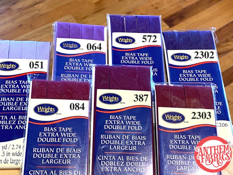 May include: Assortment of six packages of Wrights bias tape in various colors, including purple, burgundy, and navy blue. Each package features the brand name Wrights and a product description, including "Bias Tape Extra Wide Double Fold" and the corresponding product number.